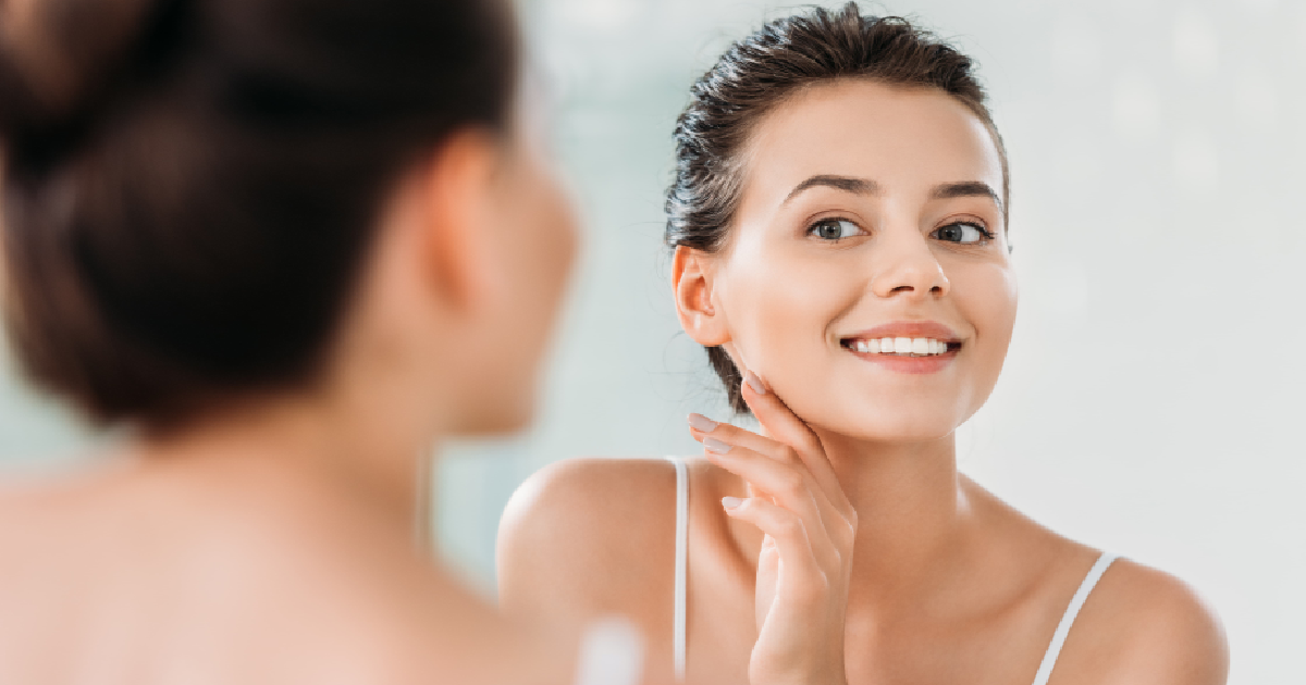 Woman smiling at her reflection in the mirror with clear, radiant skin after receiving IPL treatments in Tampa, FL.